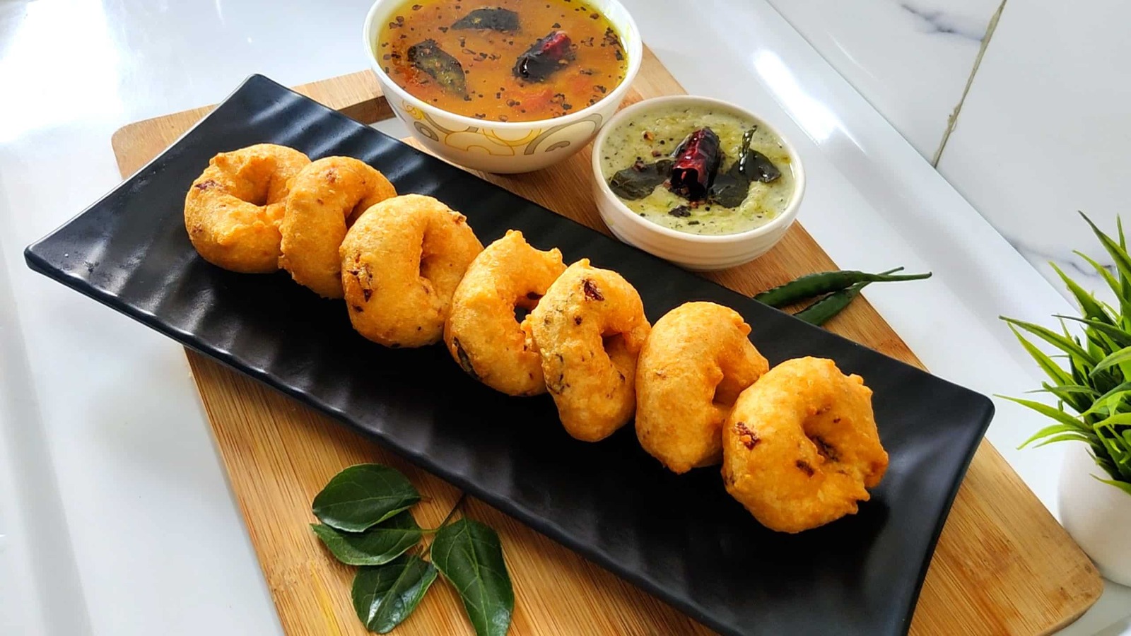 Sambar Vada – golden lentil fritters soaked in aromatic South Indian sambar, garnished with onions and coriander.